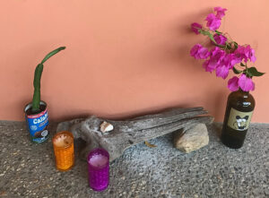 Homemade altar for incense and decoration. Large piece of wood, stones, purple and orange candles, a cactus planted in coconut milk can and flowers in a wine bottle.