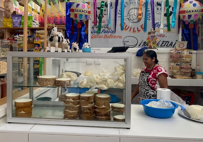 Cheeses and Oaxacan woman at a colorful cheese stand inside Mercado Sanchez Pascuas.