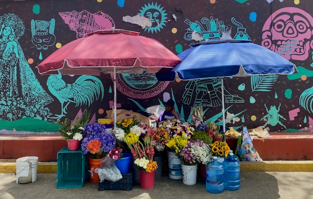 Flower vendor with many colorful flowers in front of a colorful mural at Mercado Sanchez Pascuas.